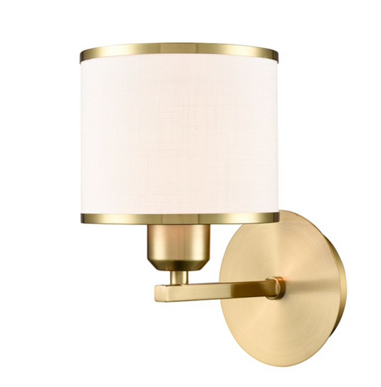 A modern wall-mounted sconce with a cylindrical white fabric shade, brushed gold metal frame, and a round brushed gold wall plate, shown against a plain white background.
